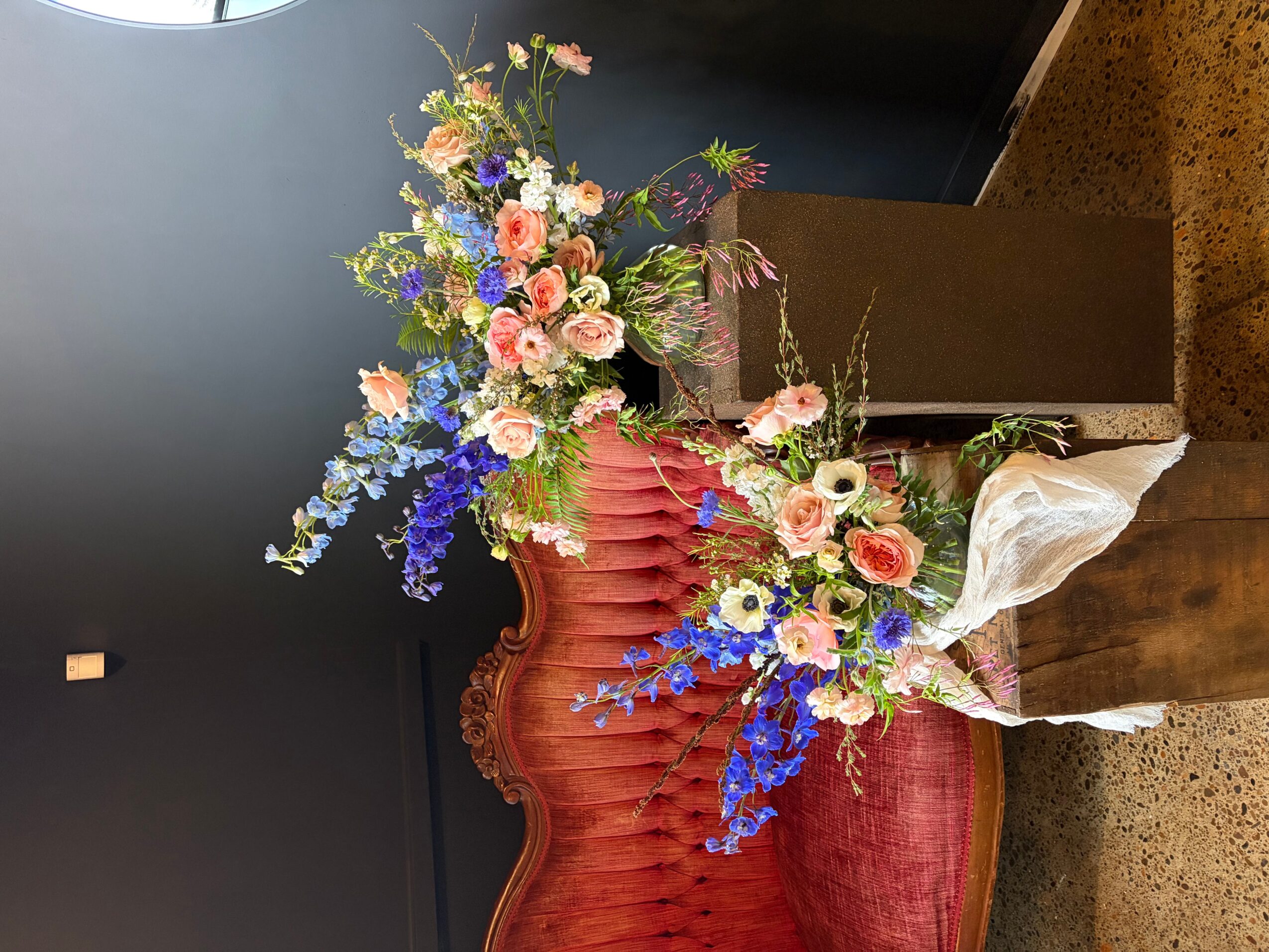 Vase with pink, purple, and blue flowers on a red velvet chair, with a dark background.