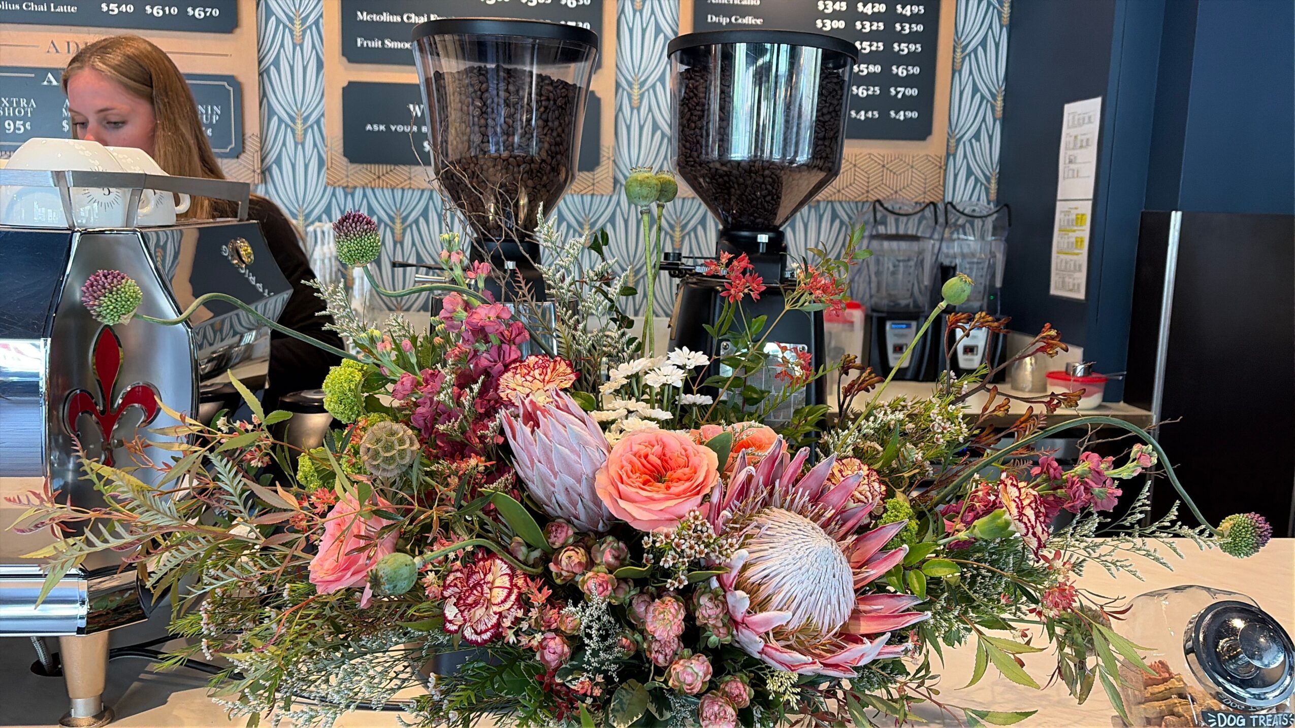 Colorful flower arrangement with pink, purple, and white flowers on a table in a cafe or restaurant setting.