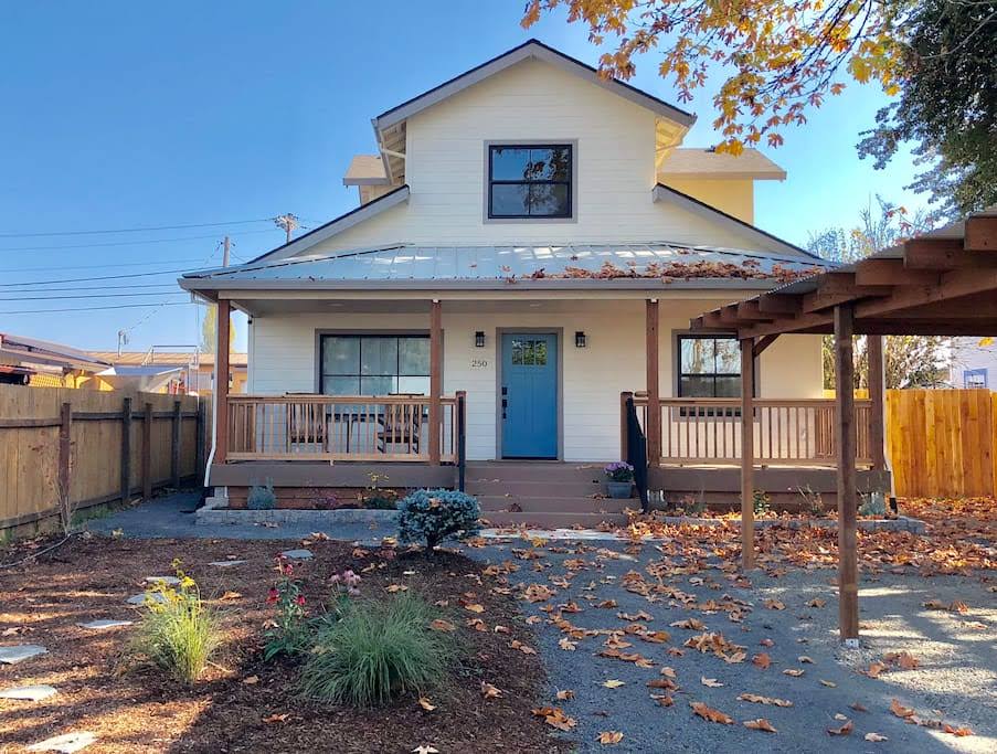 Two-story house with a blue door, front porch, and a yard with fallen leaves, under a clear blue sky.