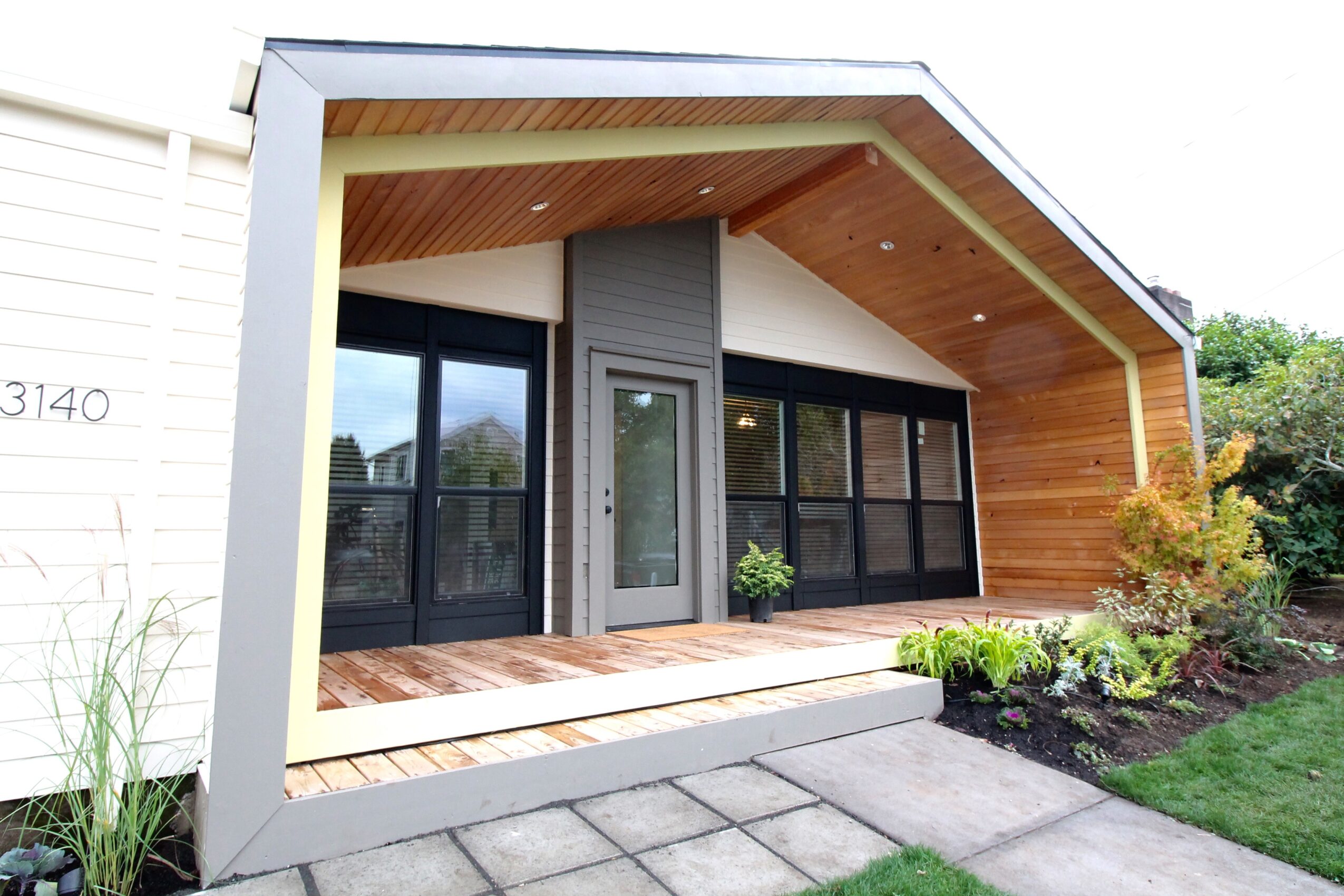Modern house with large glass doors, wooden exterior, and a small garden, viewed from the front.