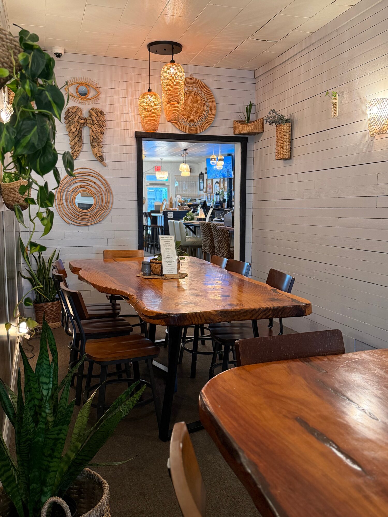 Interior of a cozy cafe with wooden tables, hanging lights, and decorative wall art, seen through a doorway.
