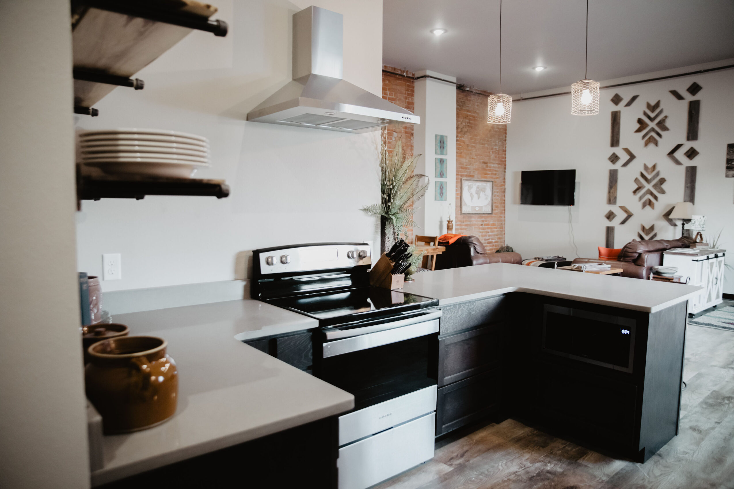 Modern kitchen with white countertops, black stove, open shelves, and a living area with a wall-mounted TV.