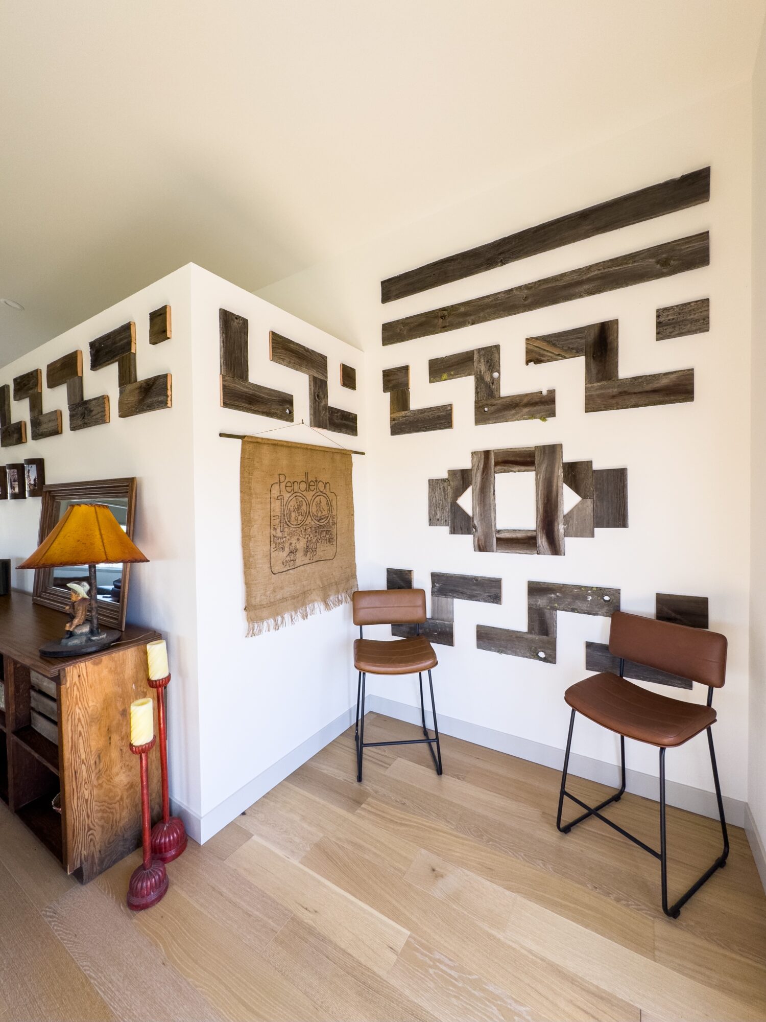 Corner of a room with decorative black and white wall patterns, two chairs, a small table, and a lamp on a wooden cabinet.