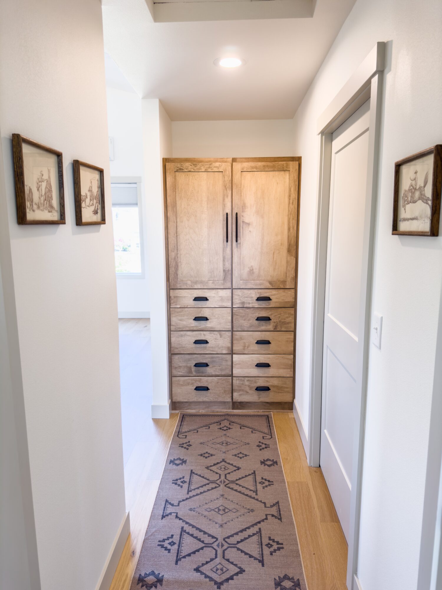Hallway with wooden cabinet, framed pictures, and a patterned rug on light hardwood floor.