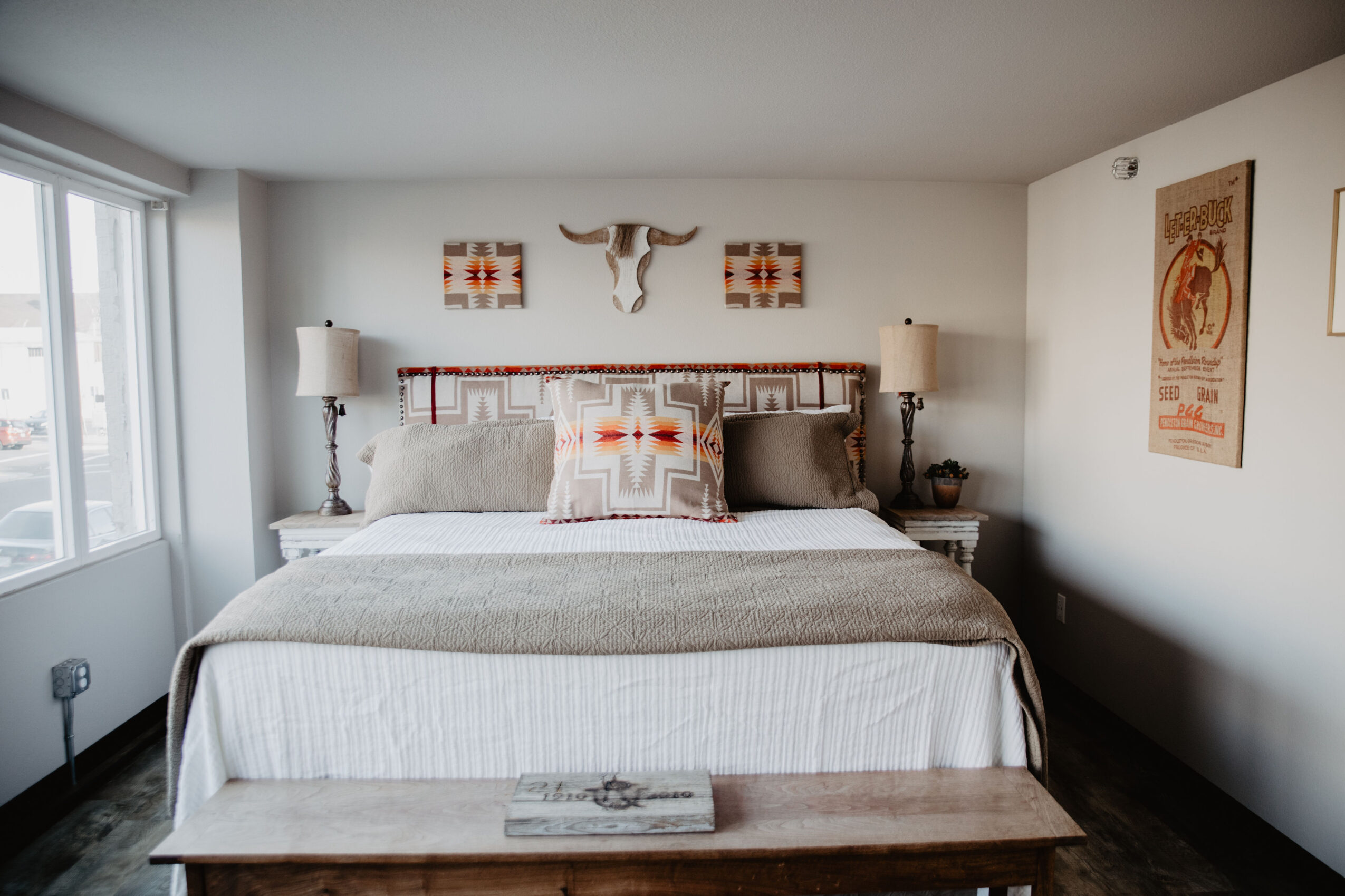 Bedroom with a large bed, decorative pillows, wall art, and a window on the left side.