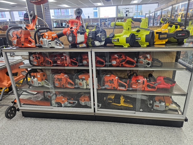 Display case with various power tools and equipment, including saws and drills, in a store setting with large windows.