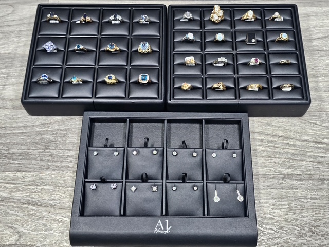 Black jewelry box with multiple compartments containing rings, earrings, and pendants on a gray surface.