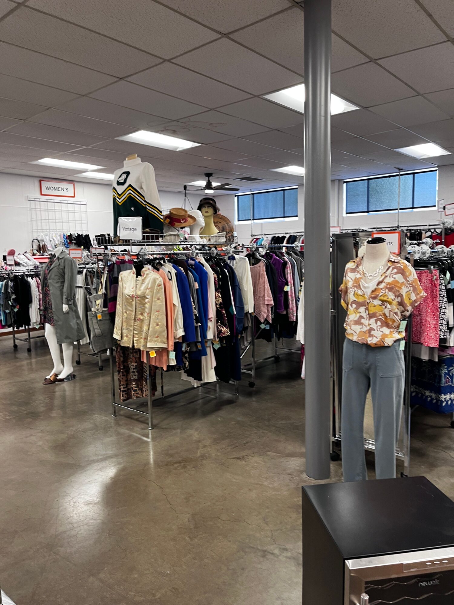 Clothing racks with various garments in a retail store, with a person browsing in the background.