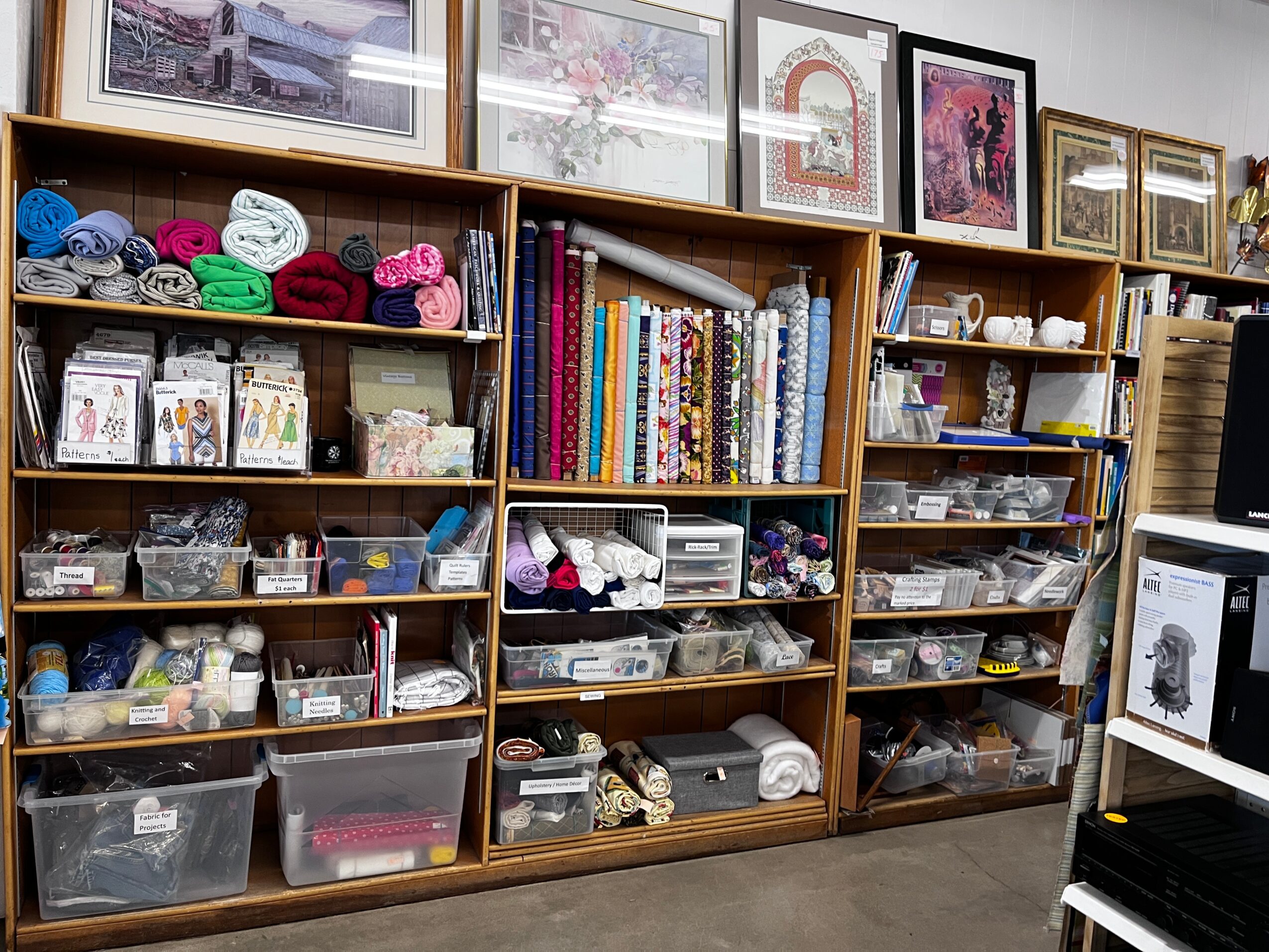 Wooden shelves filled with yarn, books, and craft supplies in a store or craft room.