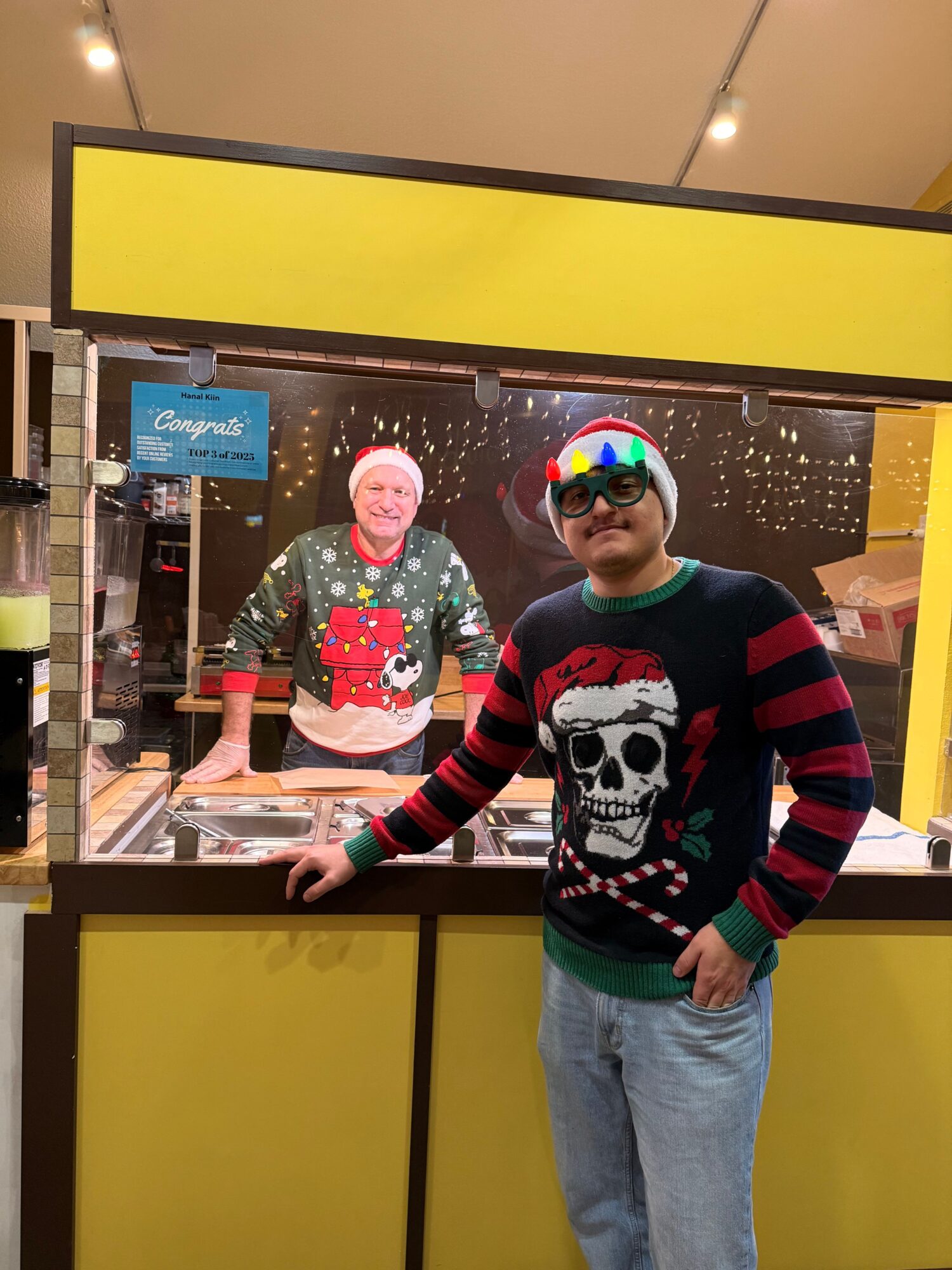 Person wearing a Christmas sweater, sunglasses, and a colorful hat, pointing at a display inside a store.