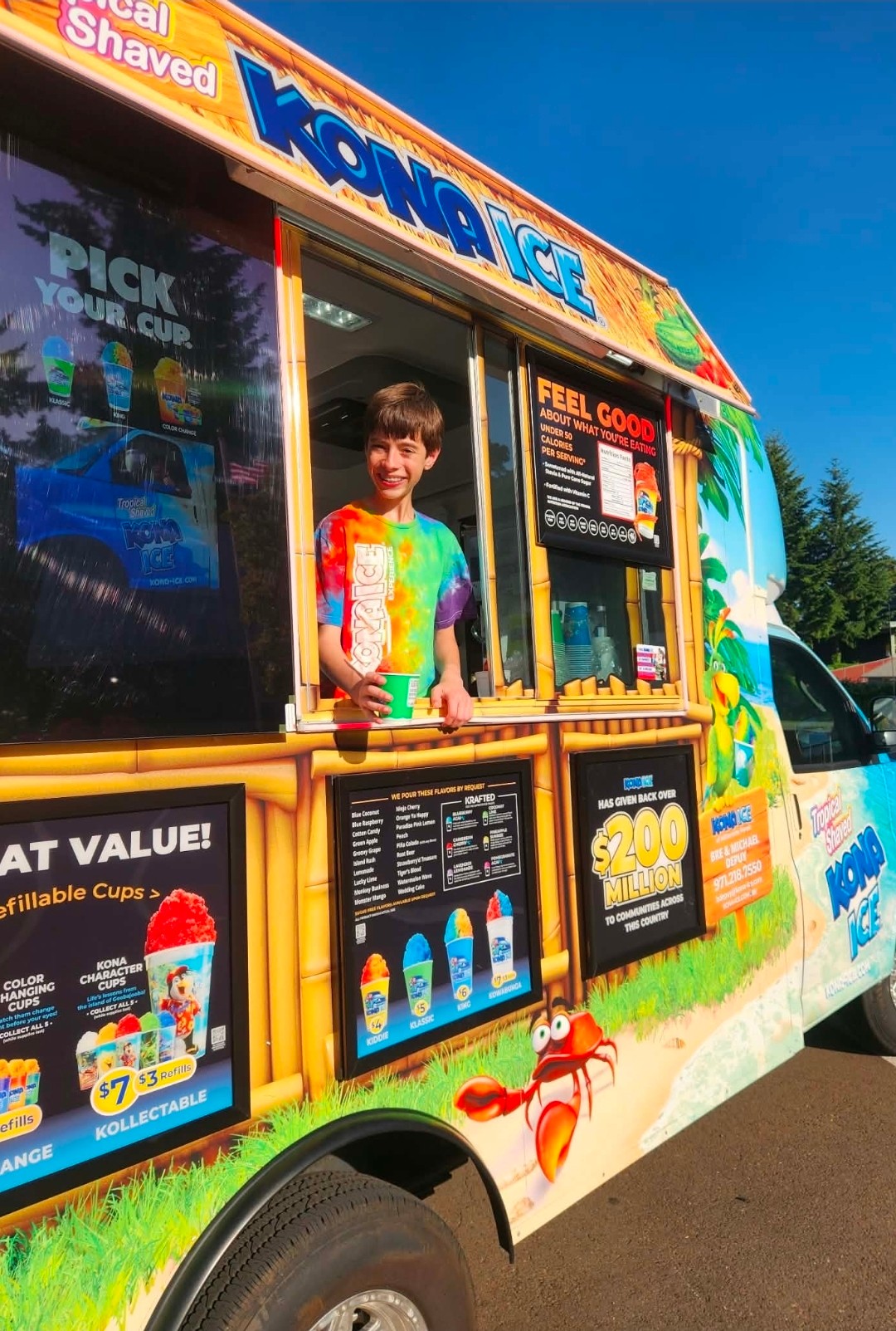Child standing inside an ice cream truck with colorful signage and menu boards, sunny day, blue sky, trees in background.