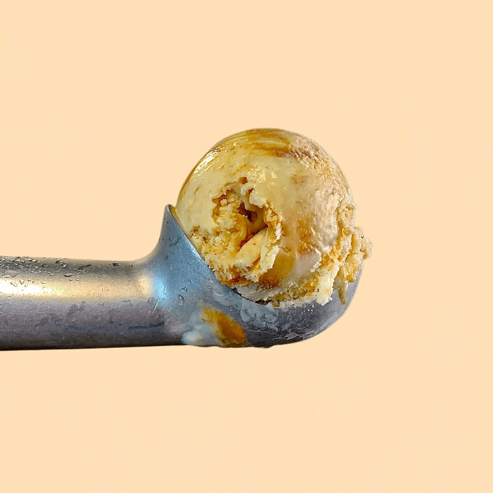 A metal spoon with a small amount of ice cream on it, against a plain light background.