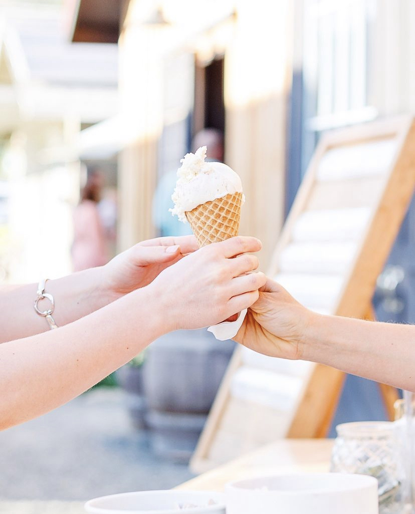 Two people exchange an ice cream cone outdoors, one holding the cone and the other reaching to take it, with blurred background.