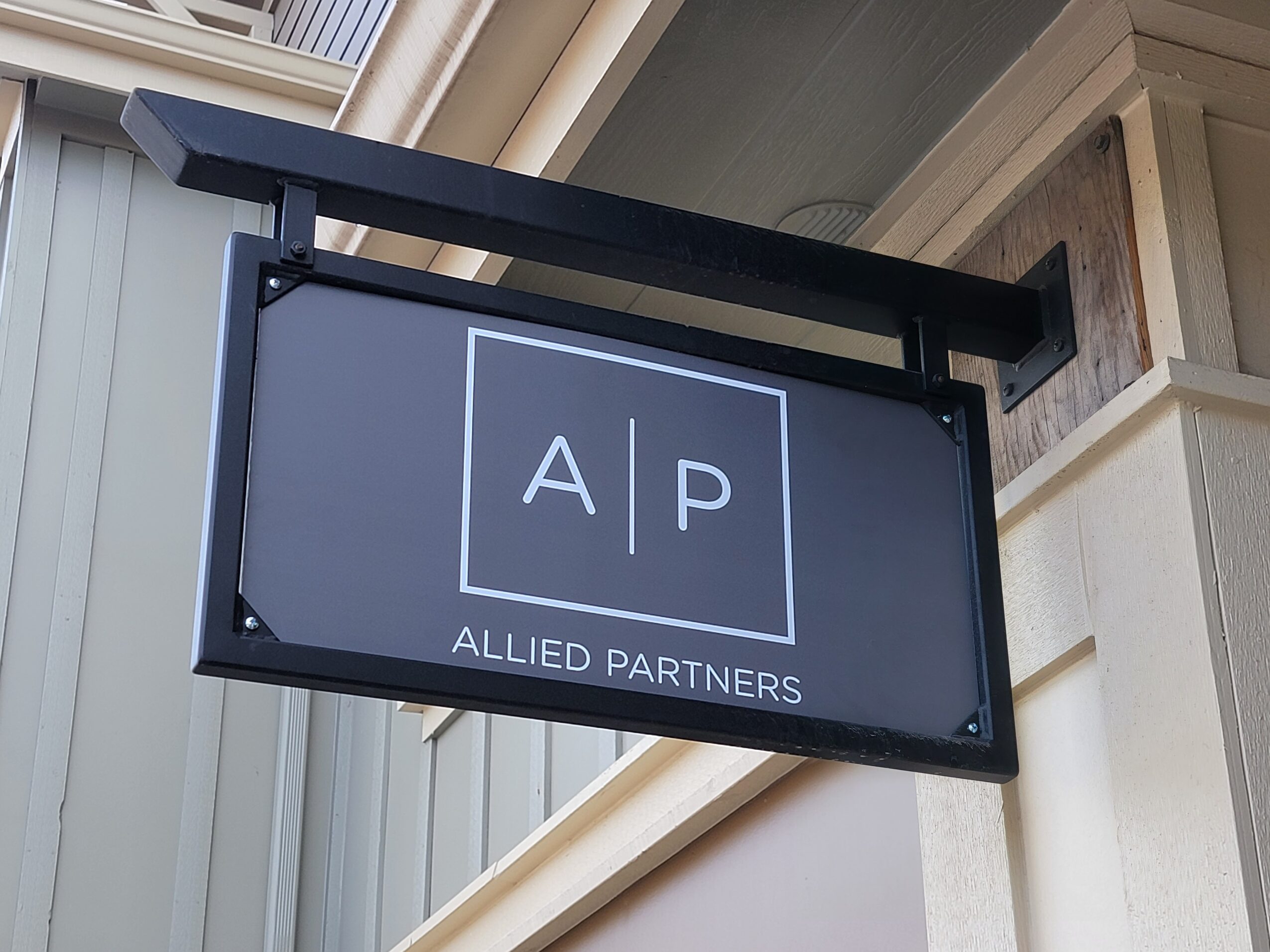Black sign with white text displaying 'A P' and 'ALLIED PARTNERS' below, mounted on a building exterior.
