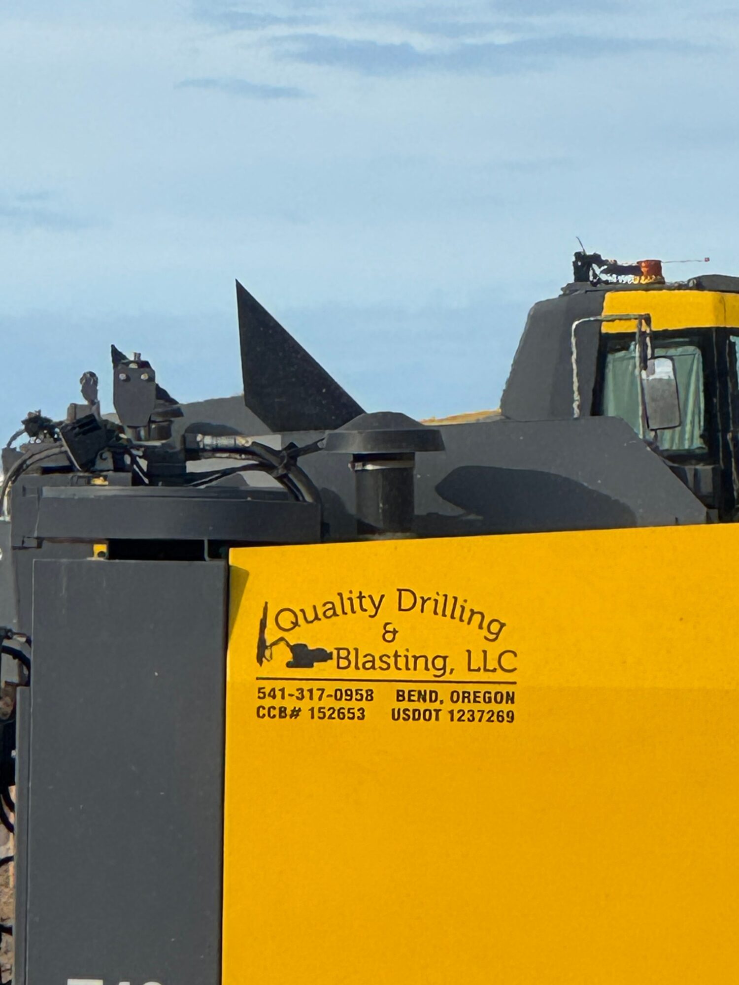 Close-up of a yellow container with black text and logo, part of a construction vehicle, against a blue sky.