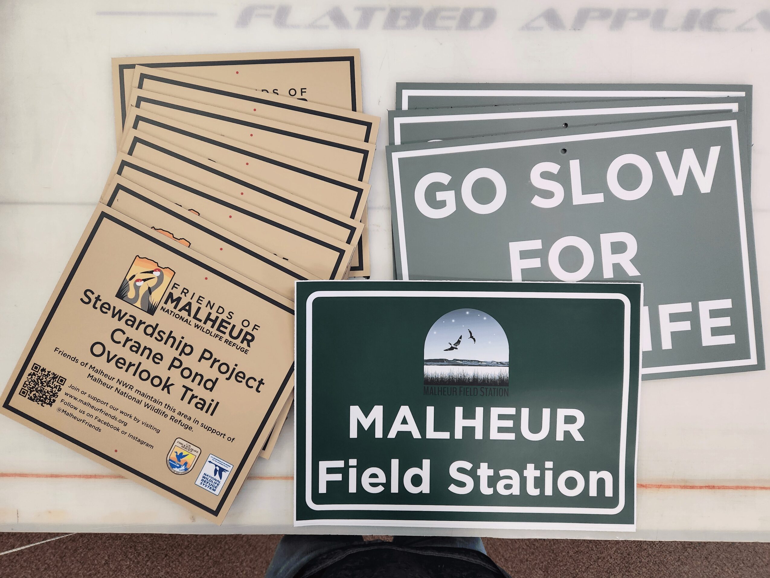 Sign for Malheur Field Station with several informational and safety signs behind it, on a white surface.