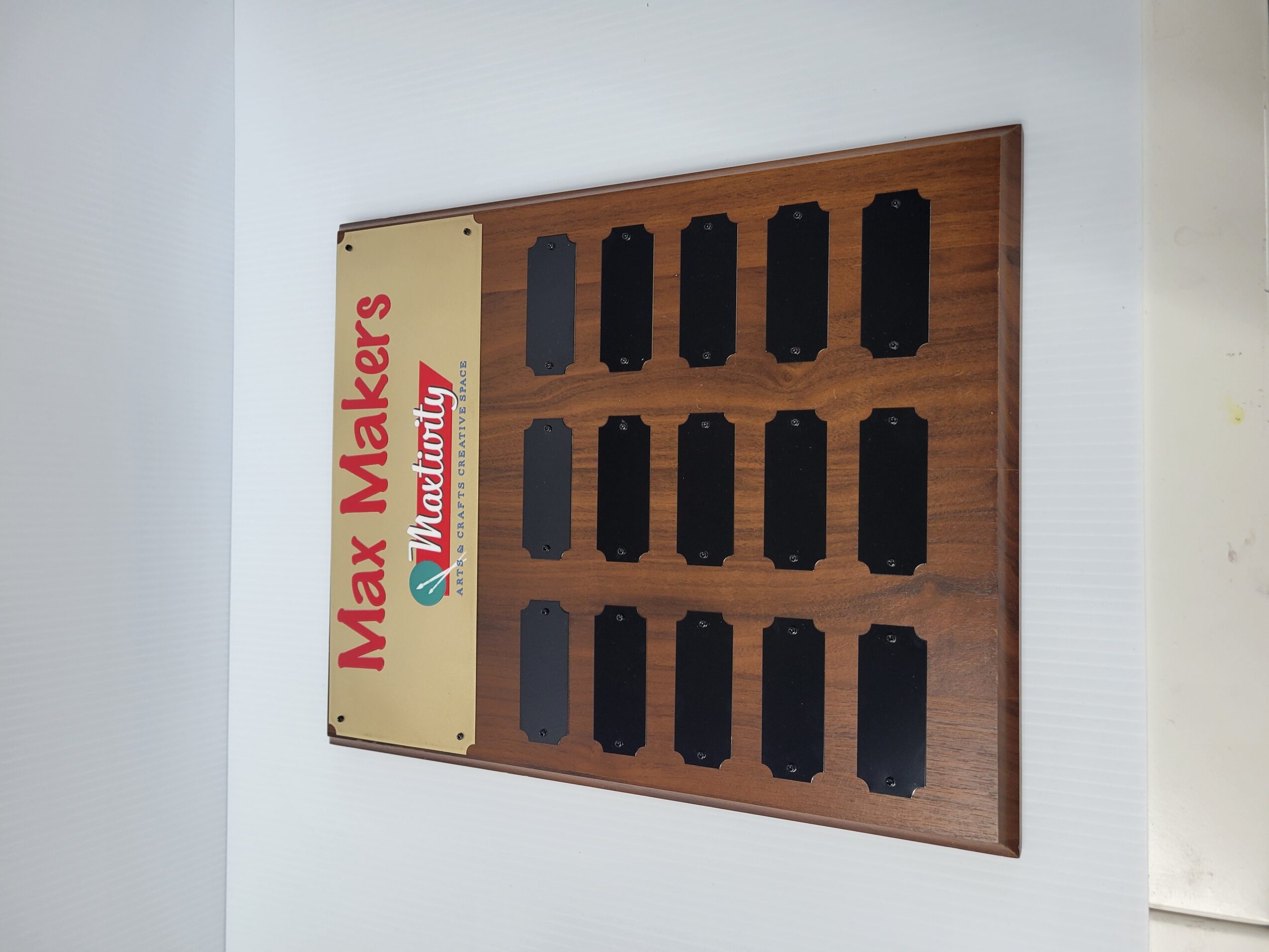 Wooden display board with black slots and a sign reading 'Max Makers' and 'Muzakurt' in red and green text.