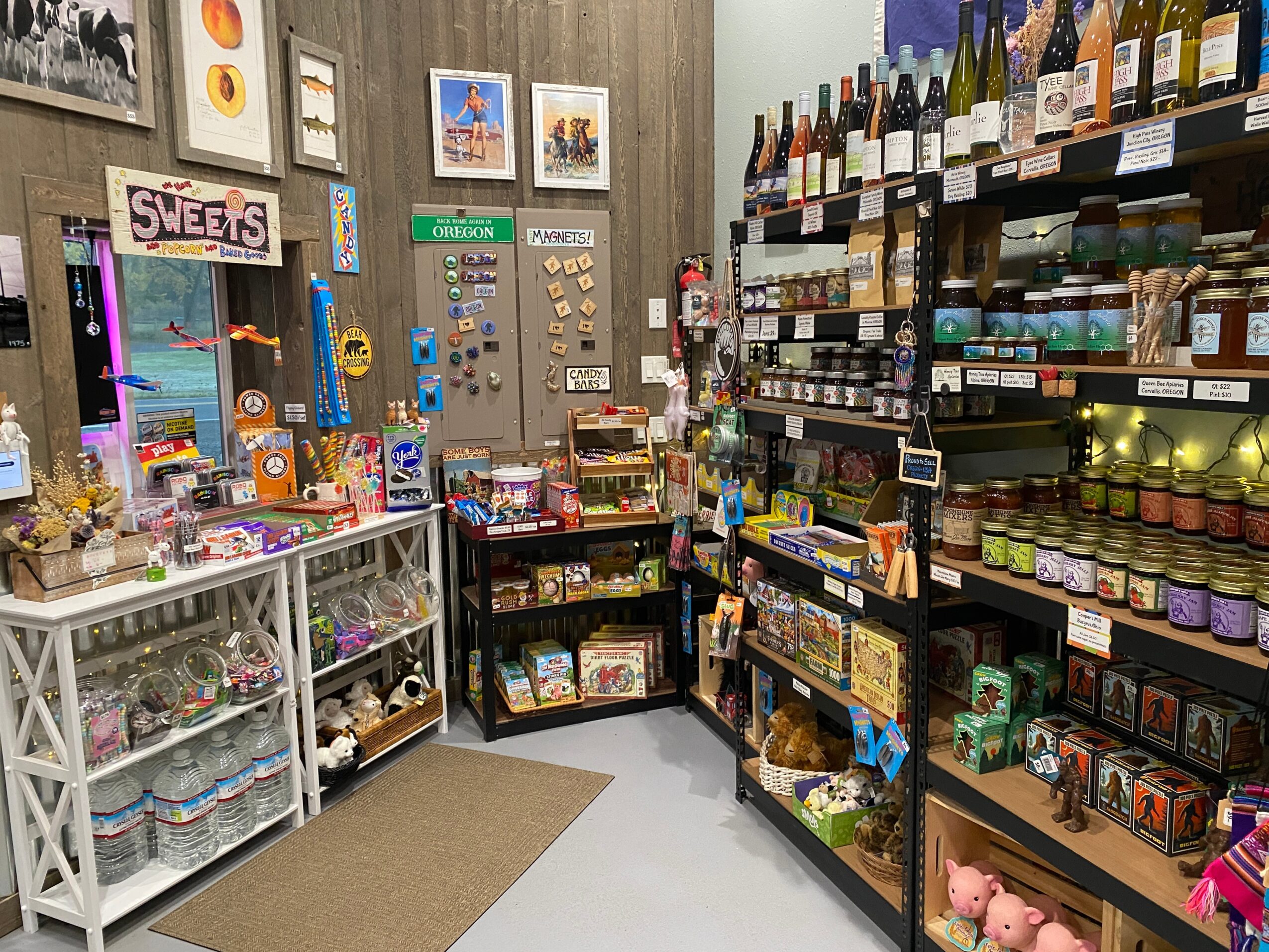 View of a store corner with shelves stocked with snacks, candies, and jars, and a display case with sweets.