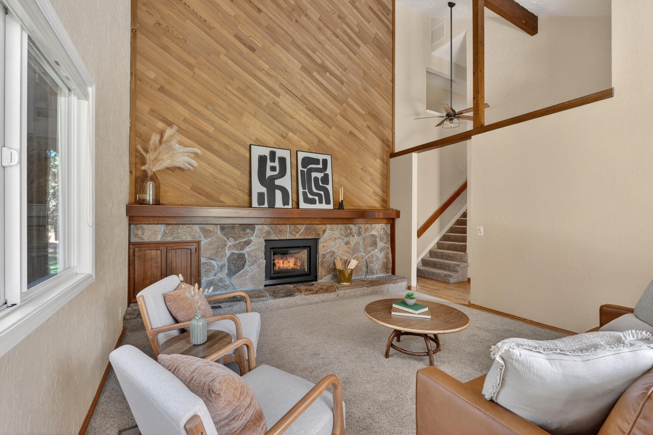 Living room with wood and stone wall, fireplace, armchair, sofa, coffee table, staircase, and window, in neutral tones.