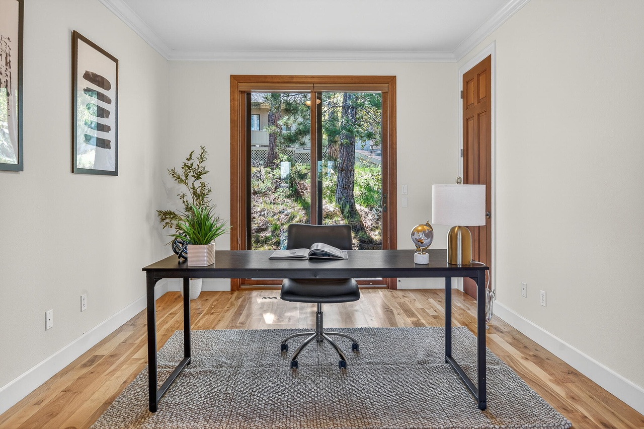 Home office with a desk, chair, window, and decor, in a bright room with hardwood floors and white walls.