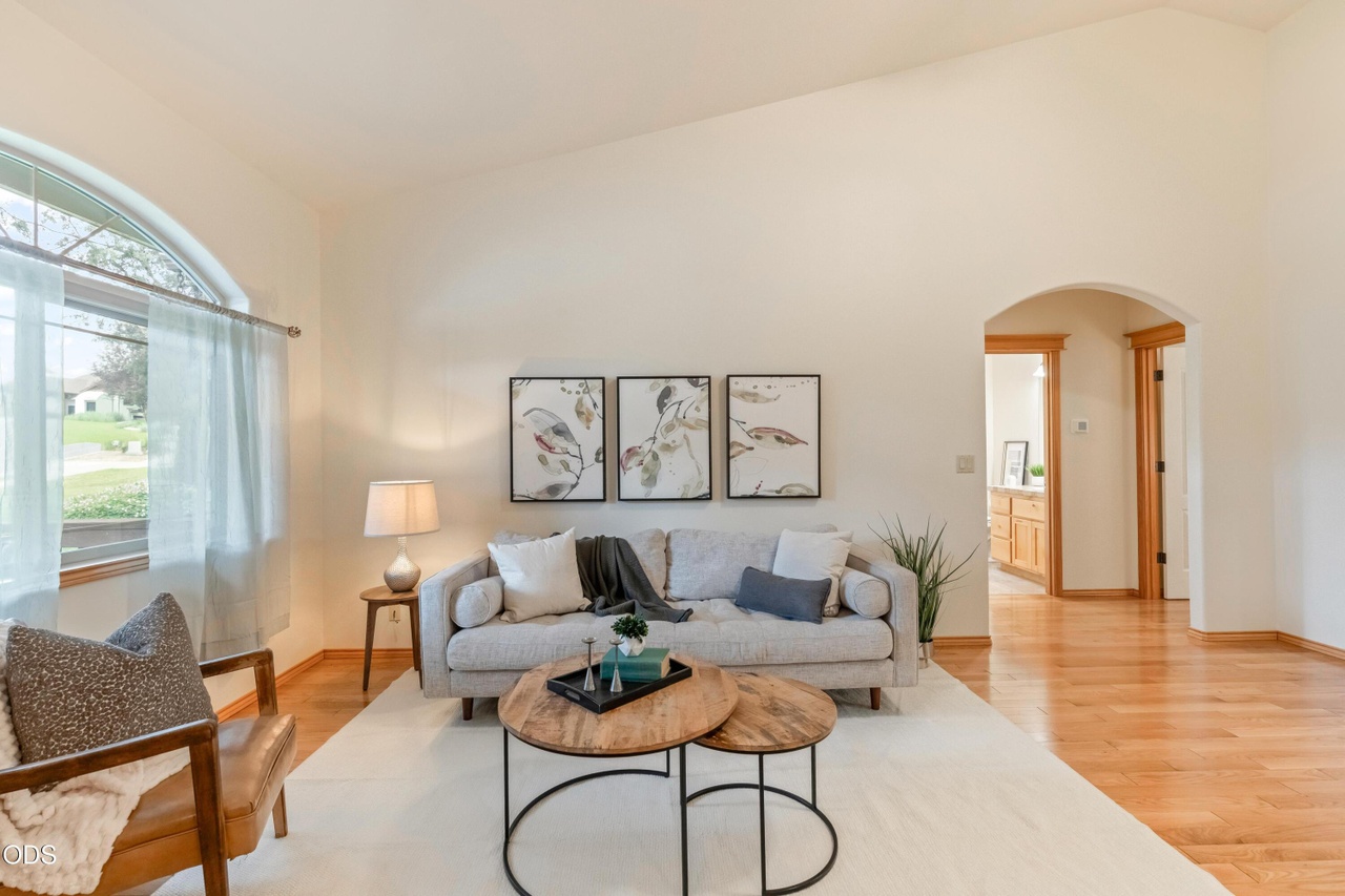 Living room with a sofa, two side tables, a lamp, and wall art, with a window and hardwood floor.
