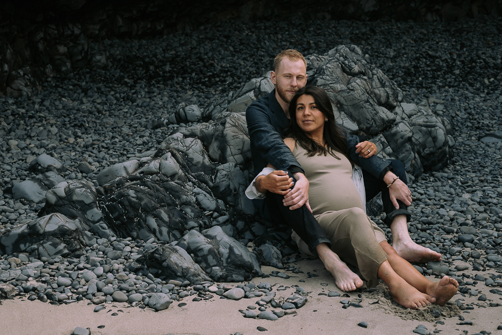 A couple sitting on rocks in a rocky landscape, with the man holding the woman from behind, both barefoot.