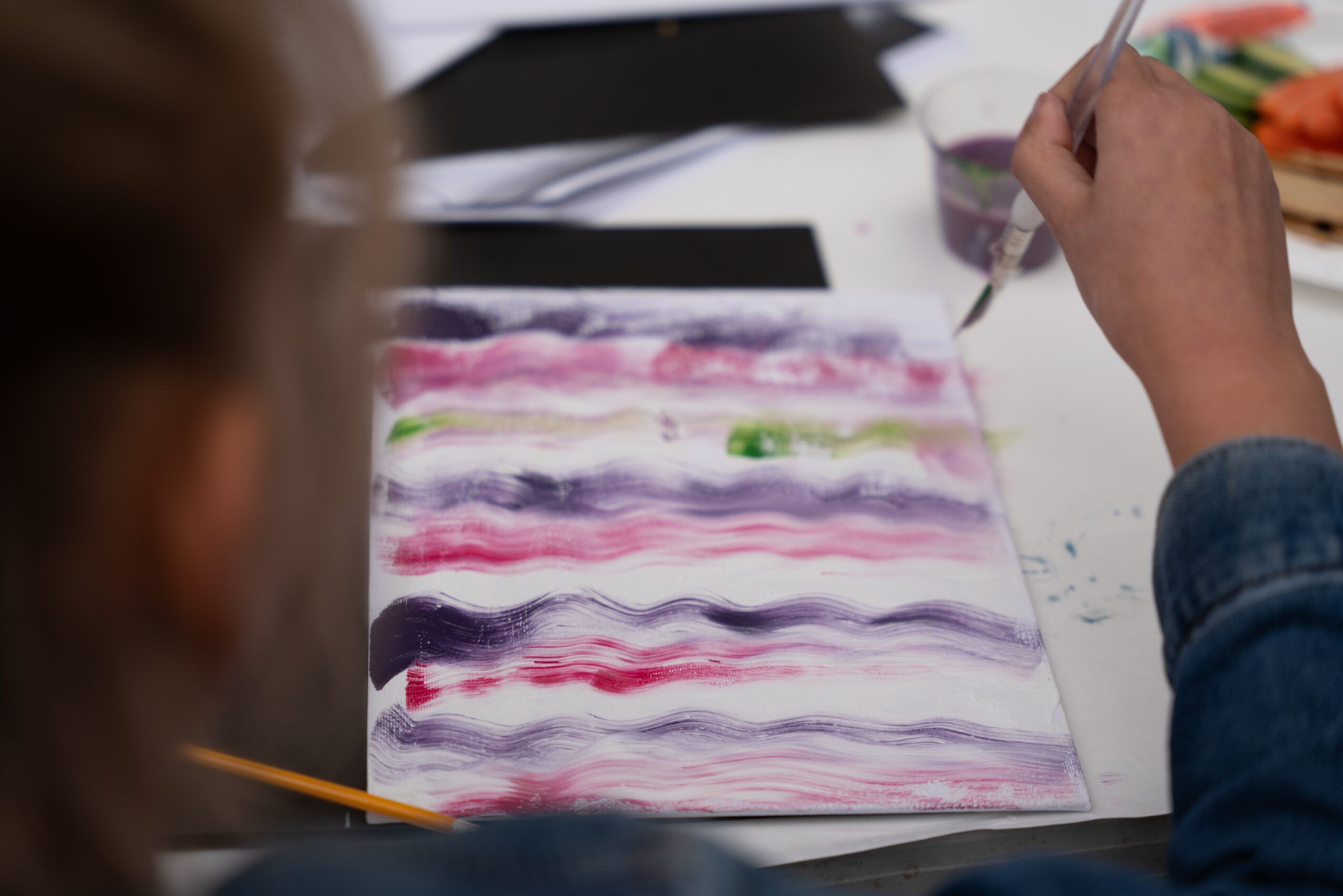 Person painting with watercolors on paper, with various colors and brushstrokes visible.