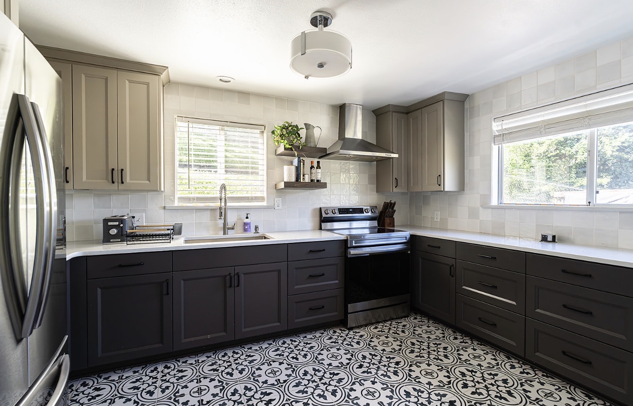 Modern kitchen with beige upper cabinets, dark lower cabinets, stainless steel appliances, and patterned floor tiles.