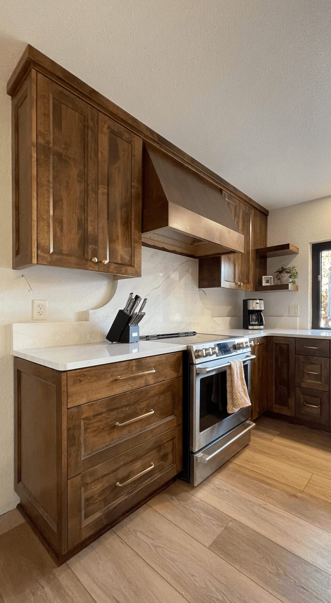 Kitchen with wooden cabinets, white countertop, stove, and small potted plant, viewed from the side.