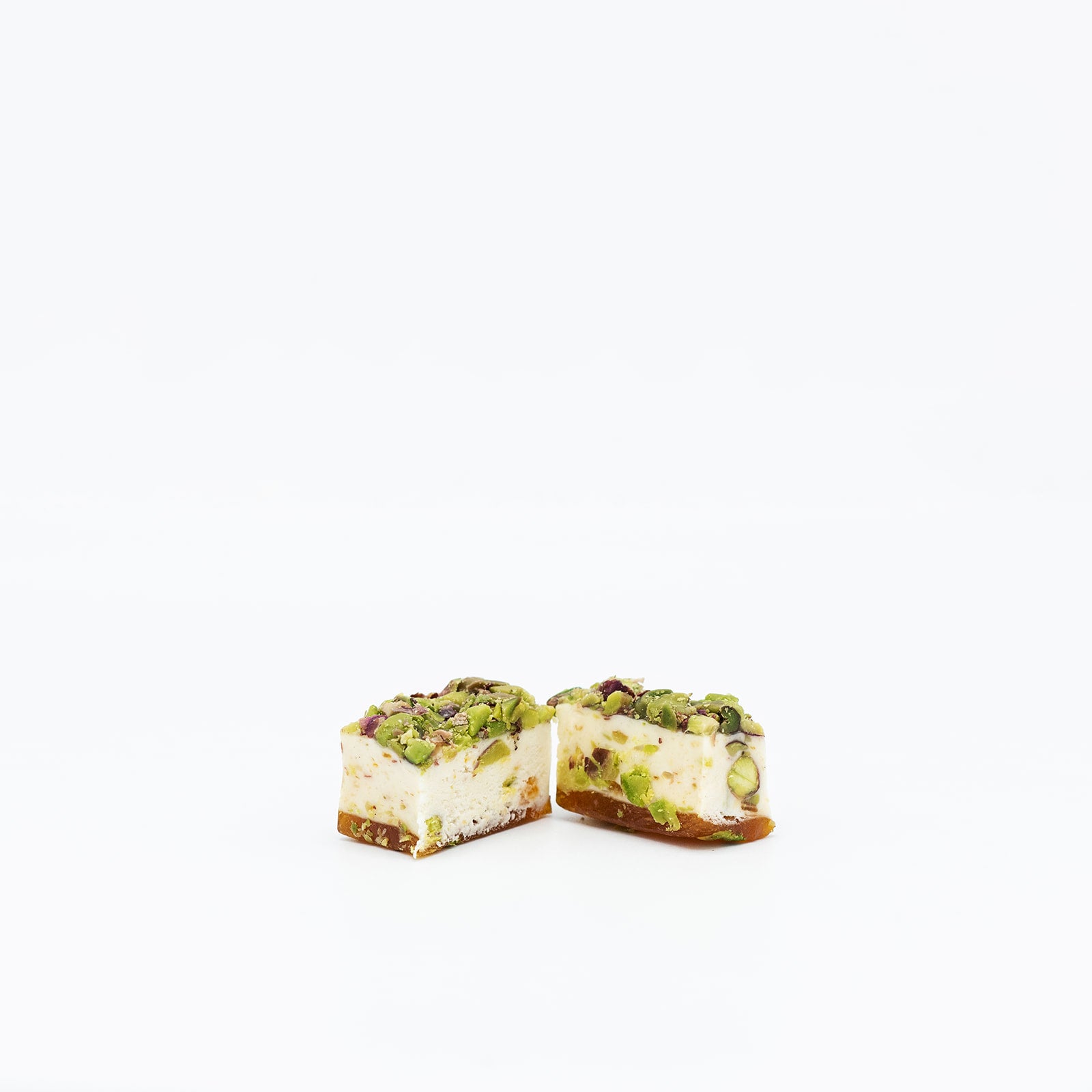 Two pieces of pistachio-flavored dessert with nuts and a creamy filling, on a white background.