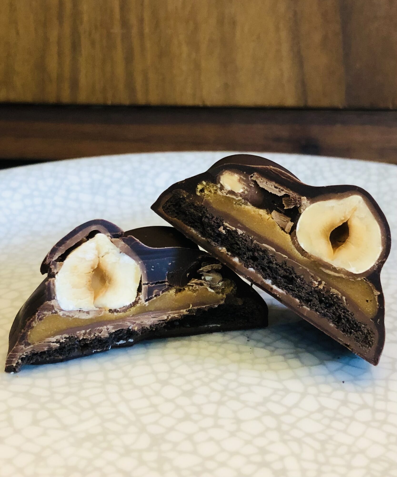 Two chocolate candies with a heart-shaped filling and a nut inside, cut in half, on a textured white surface.