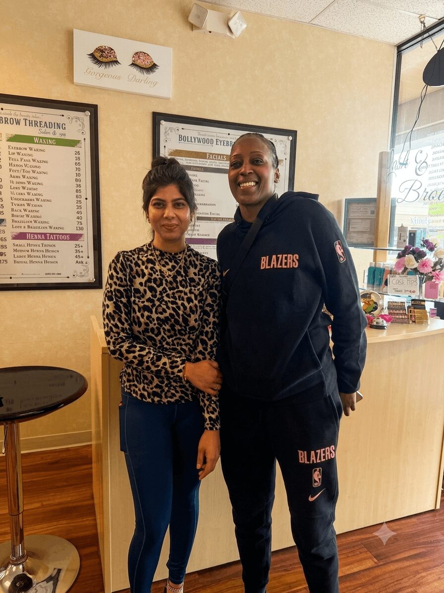 Two women standing inside a restaurant, one wearing a leopard print top and the other in a black hoodie with 'BLAZERS' written on it, smiling.