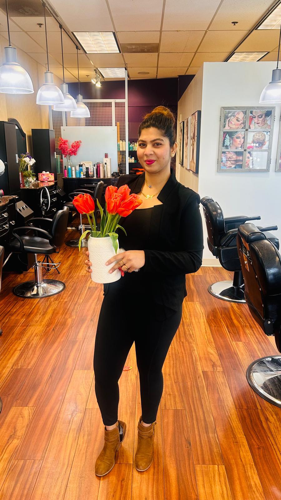 Woman holding a white pot with red tulips in a salon with black chairs and wooden floor