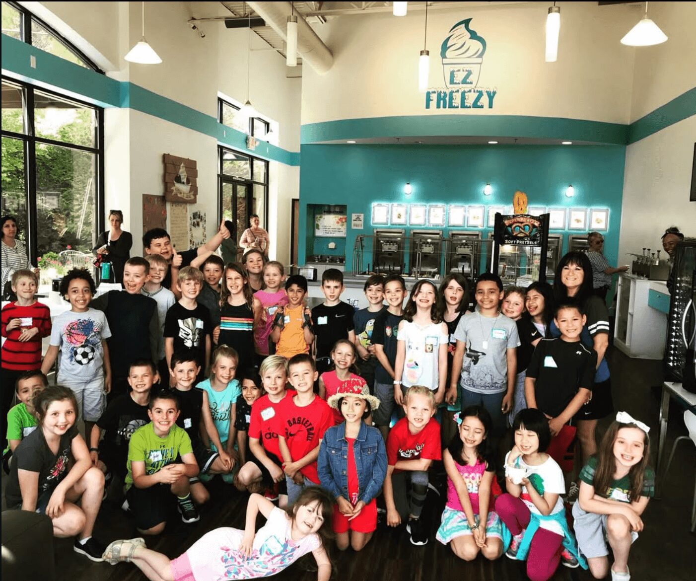 Group of children in a store with shelves and a sign that says EZ FReezy, some children are raising their hands.