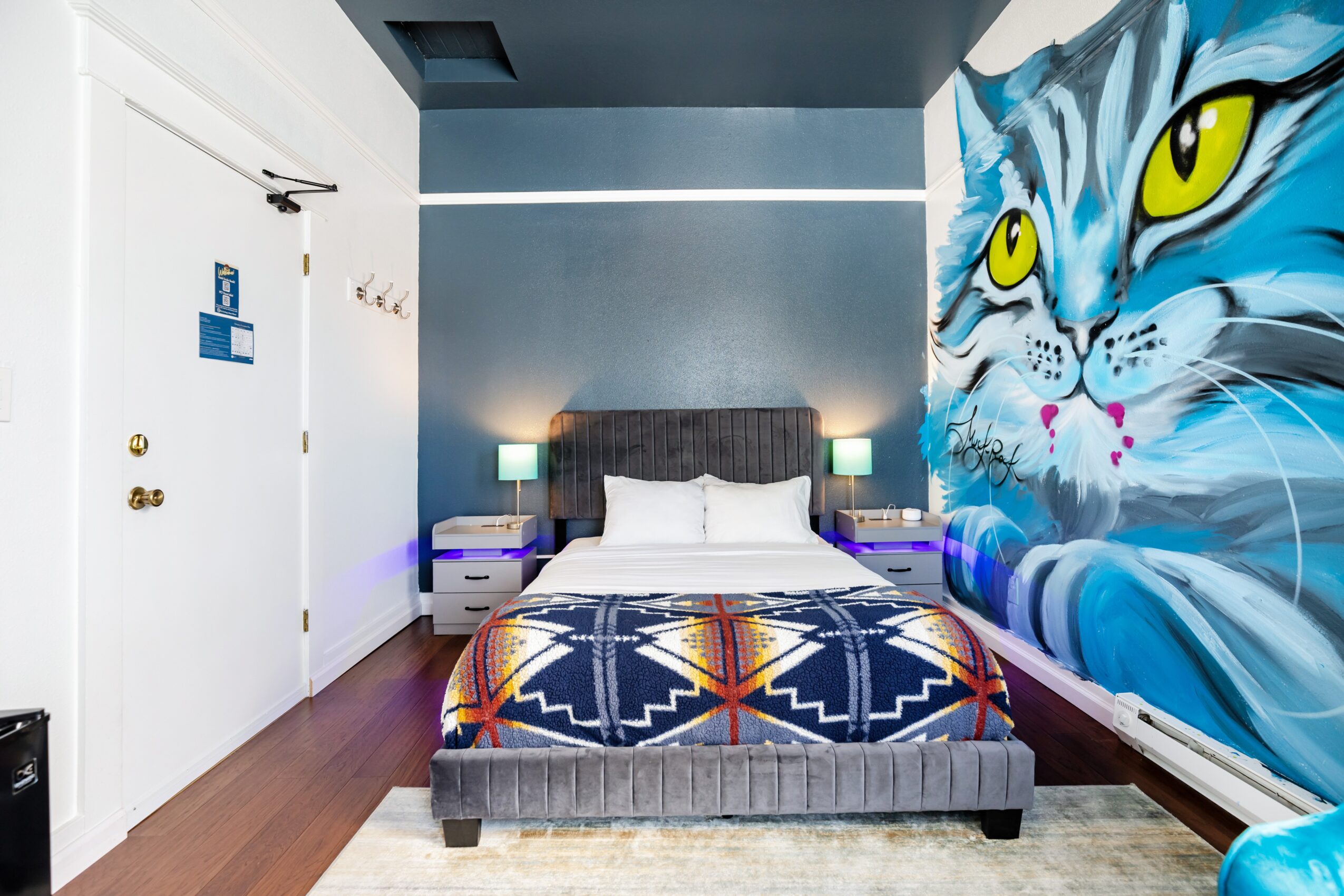 Bedroom with a bed, nightstands, and a large mural of a blue cat's face on the wall.