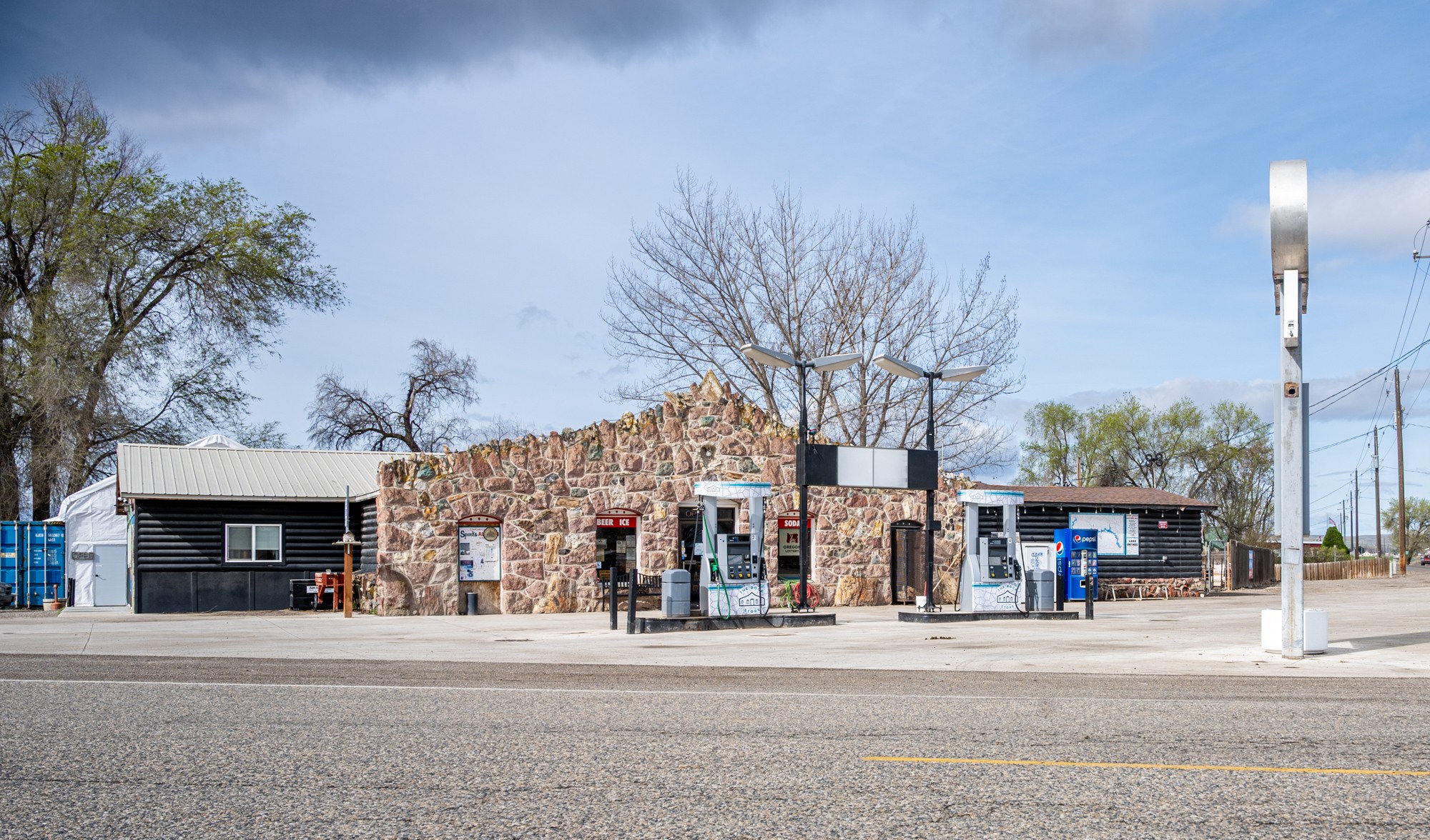 Small brick building with two blue vending machines outside, trees in background, clear sky, and a sidewalk in front.