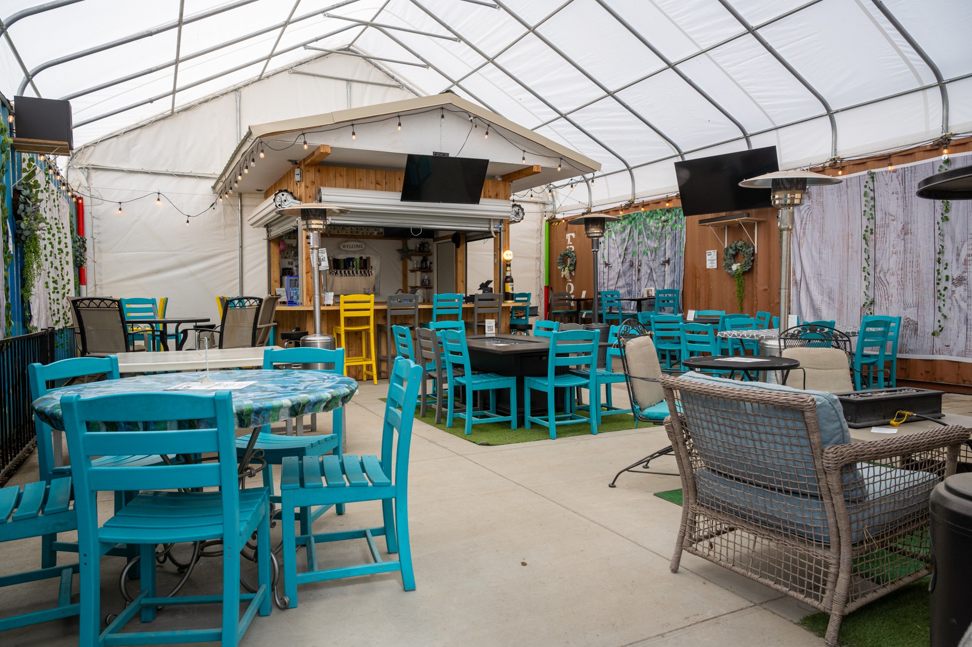 Indoor dining area with blue and gray chairs, tables, and a stage with a TV, under a curved ceiling.