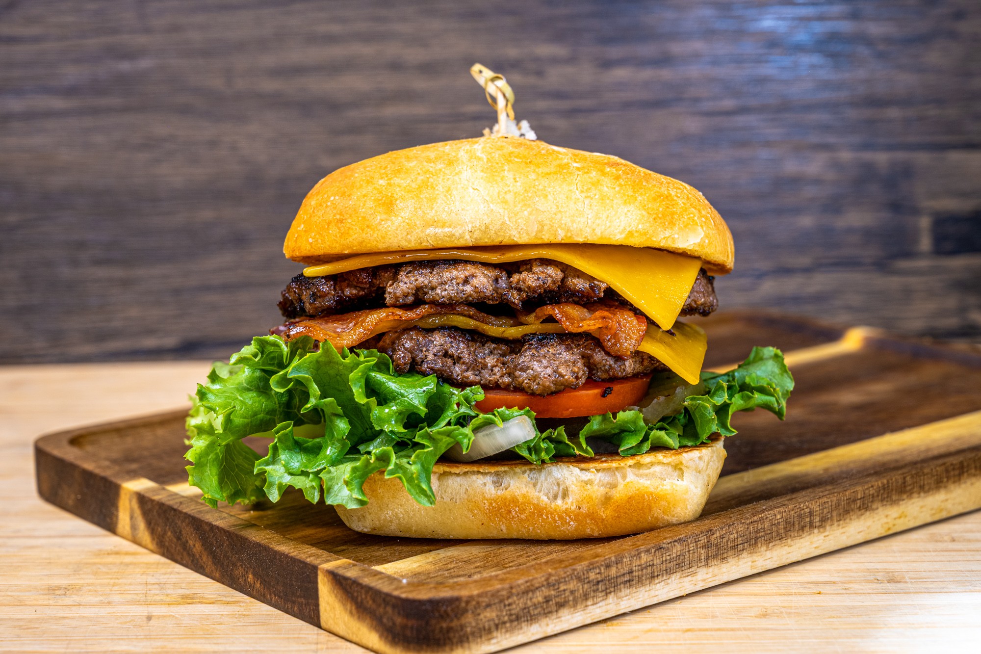 A burger with lettuce, tomato, cheese, and beef patties on a wooden board.