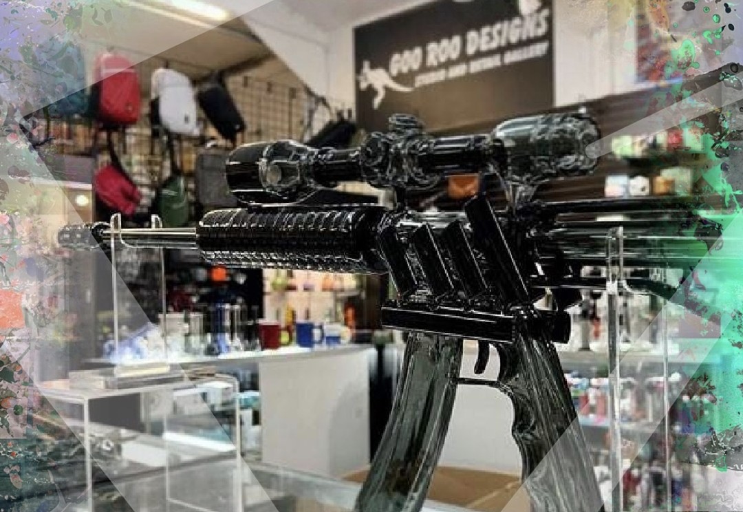 Black firearm replica displayed on a glass stand in a store, with shelves and merchandise in the background.