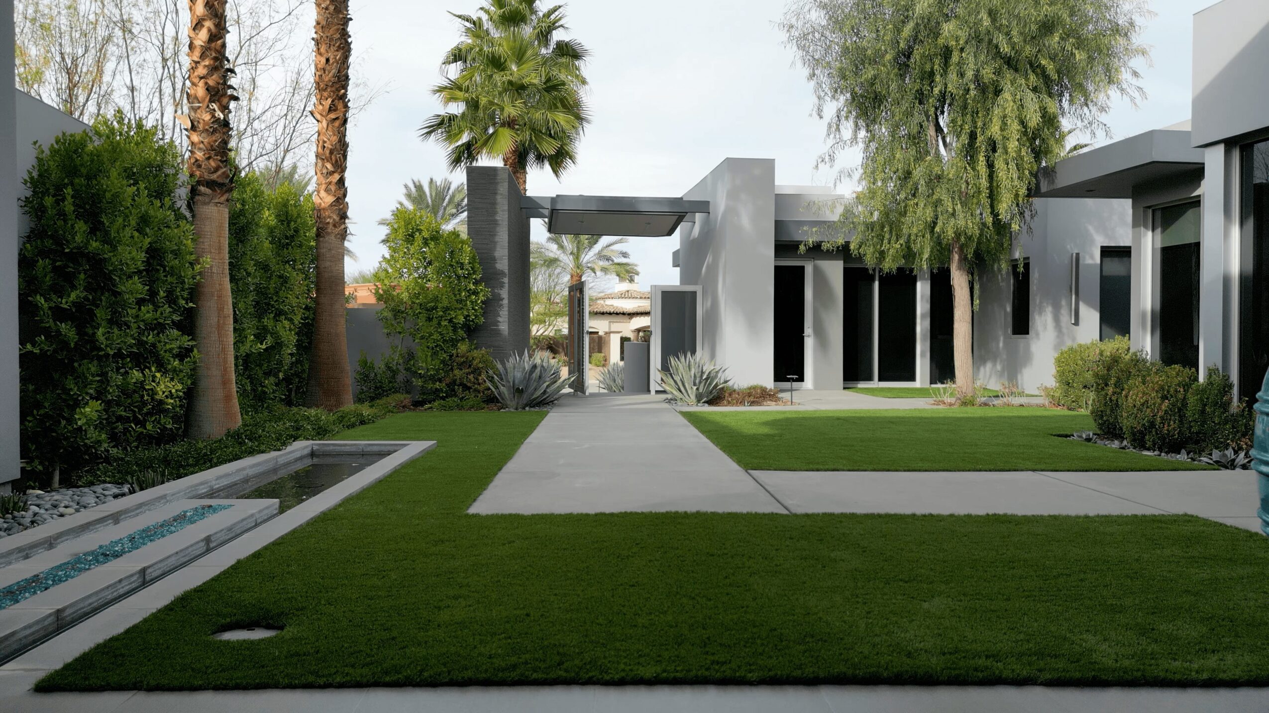 Modern residential area with a walkway, green lawn, trees, and contemporary buildings in the background.