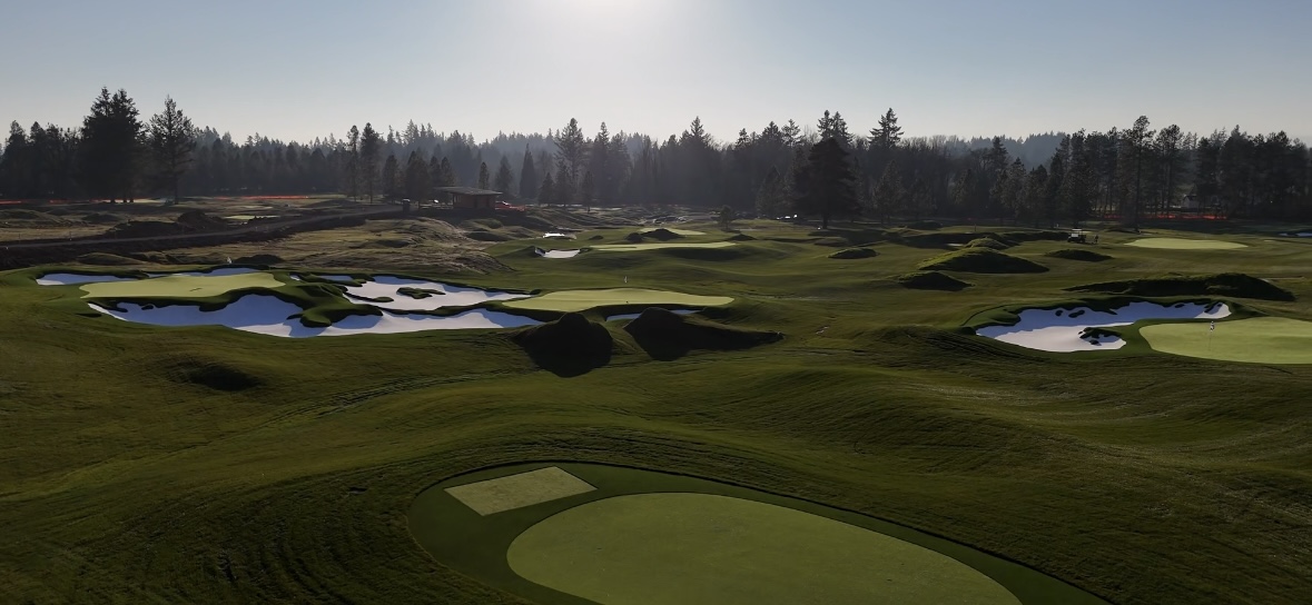 Golf course with green fairways, sand traps, and water hazards under a clear sky.