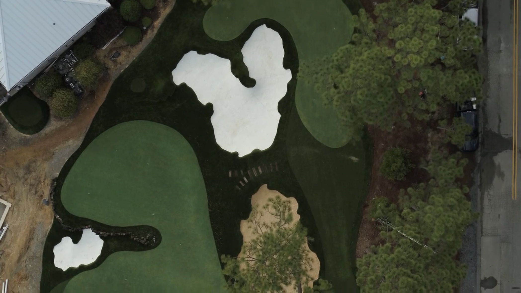 Aerial view of a golf course with sand traps, water hazards, and trees surrounding the fairways.