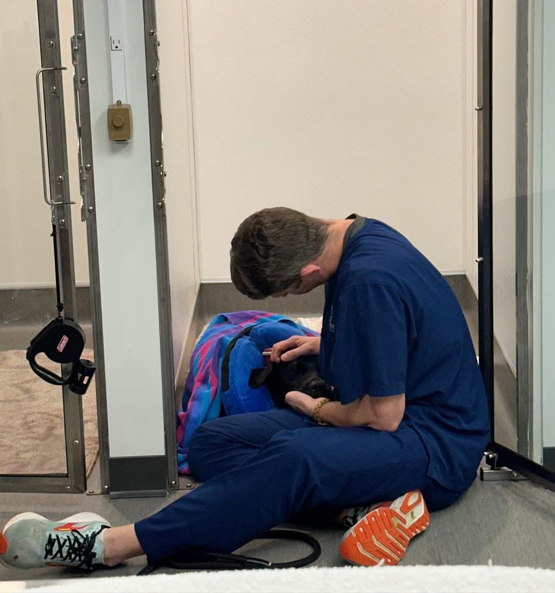 Person sitting on the floor, leaning forward, with a colorful bag nearby, in a clinical setting.