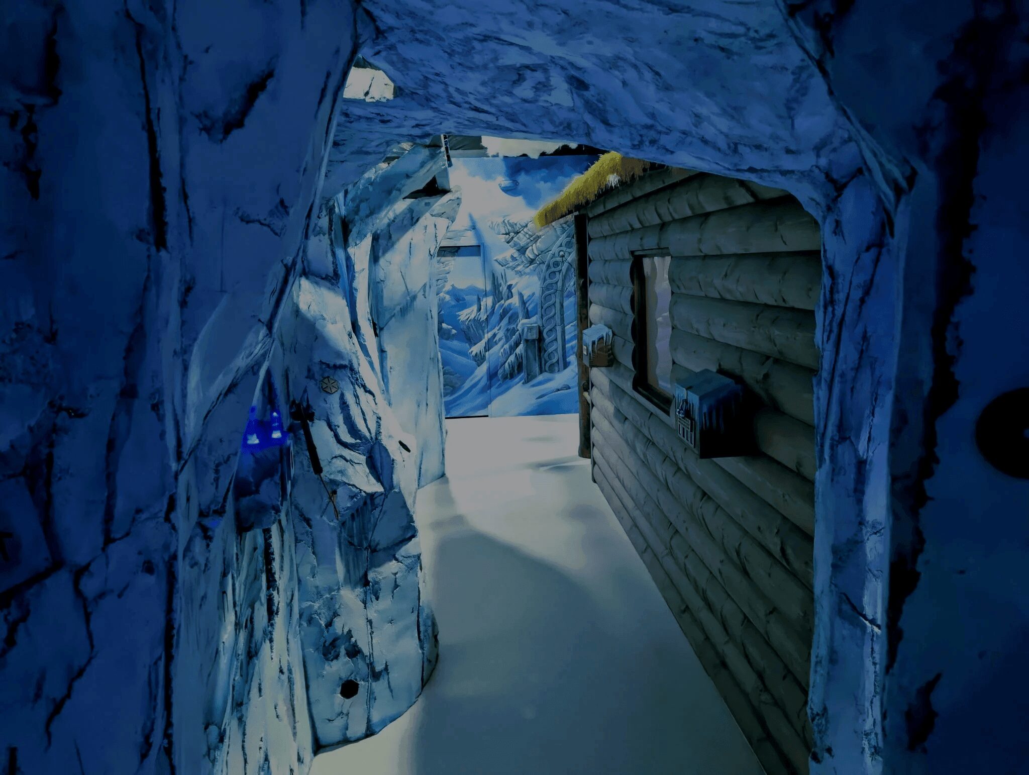 Snow-covered pathway between icy walls and a wooden cabin, with snow on the ground and icy formations on the sides.