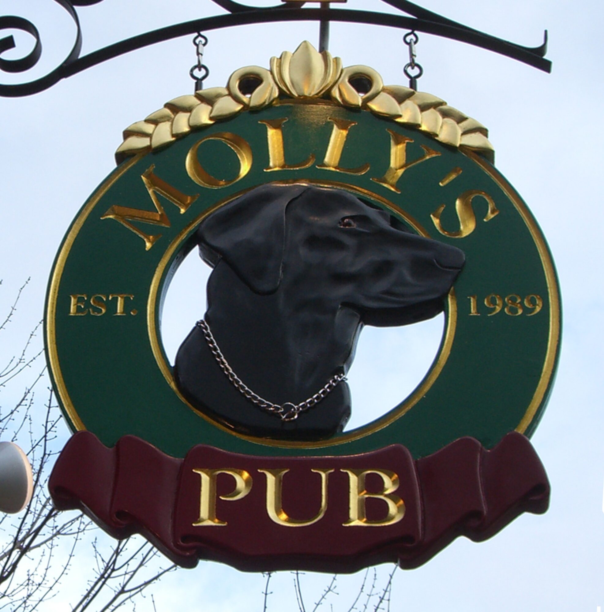 Sign for Molly's Pub featuring a black dog wearing a chain collar, with green and gold colors, and a maroon banner reading 'PUB'.