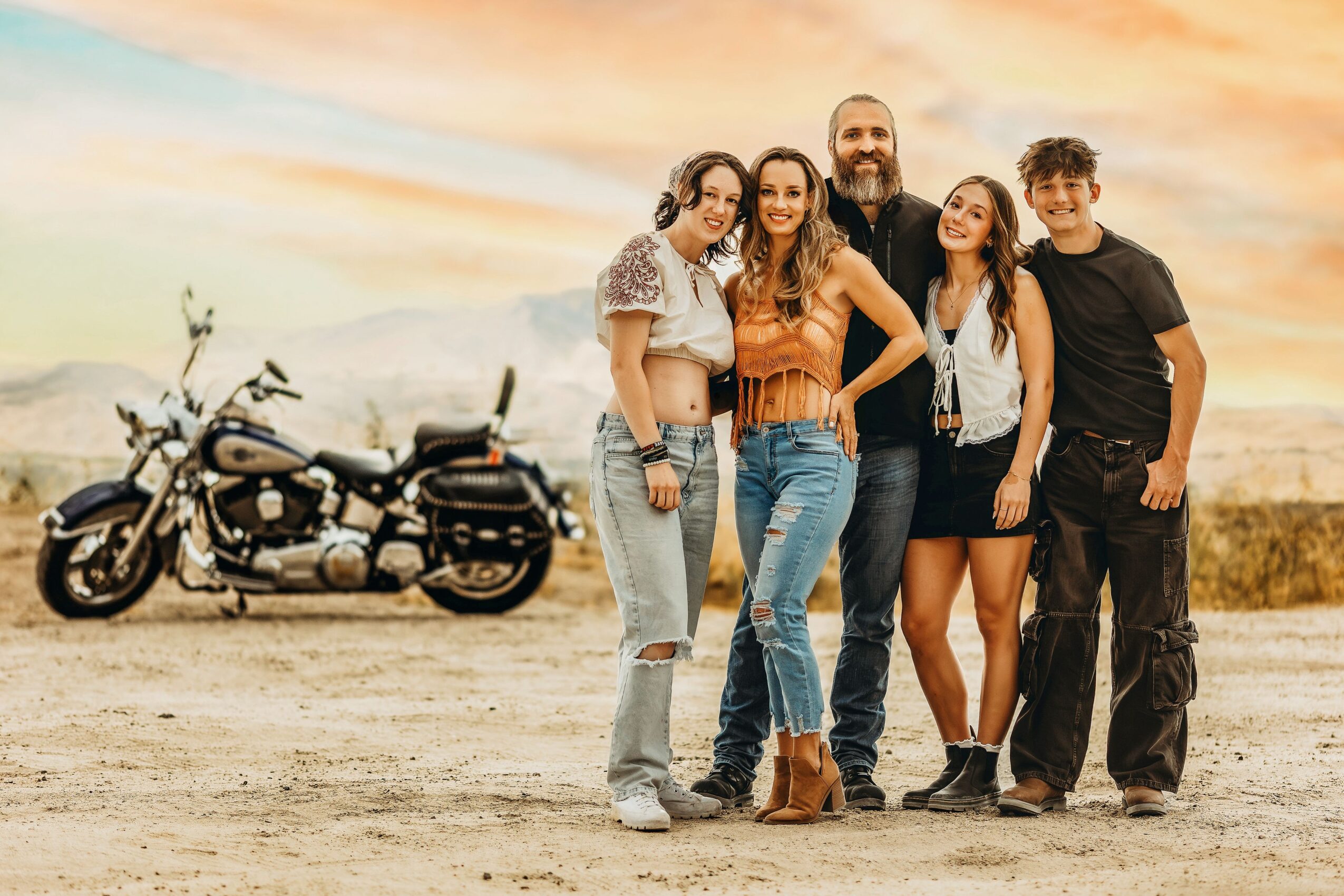 Group of five people standing outdoors with a motorcycle in the background during sunset.
