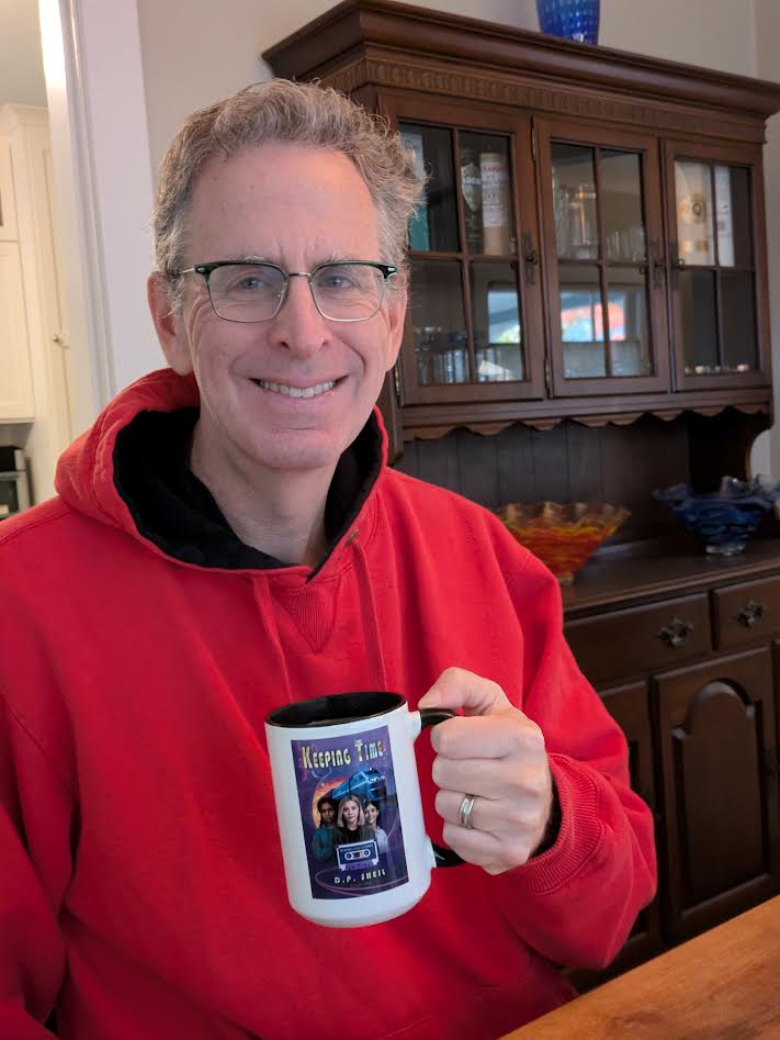Man with glasses and gray hair smiling, holding a mug with a space-themed design, in a room with a wooden cabinet.