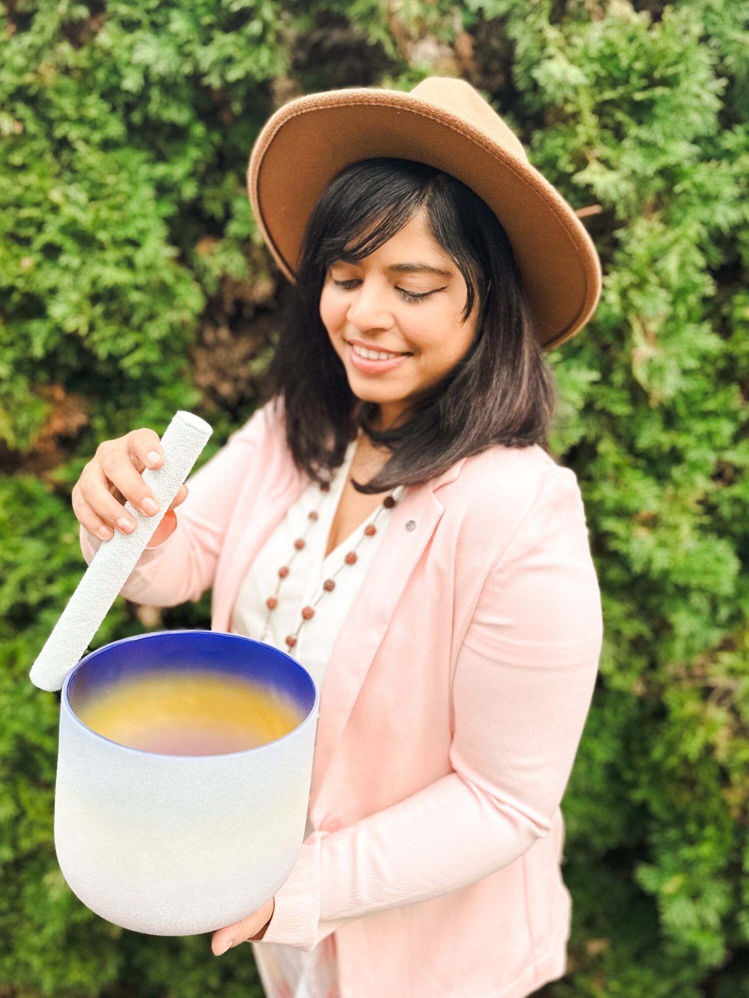 Young woman with a hat holding a large bowl outdoors, smiling, surrounded by green foliage.