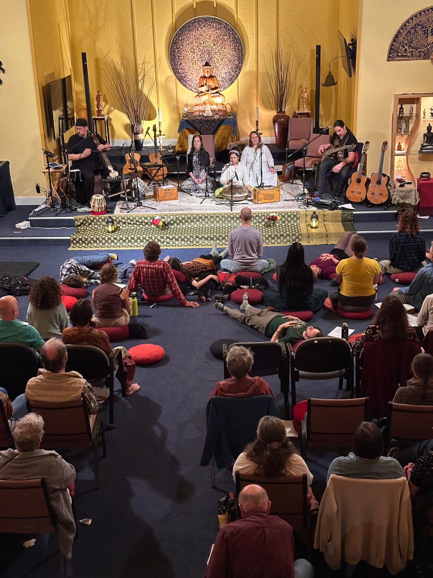 People gathered in a church with a stage, musical instruments, and a large cross on the wall, during a service or event.