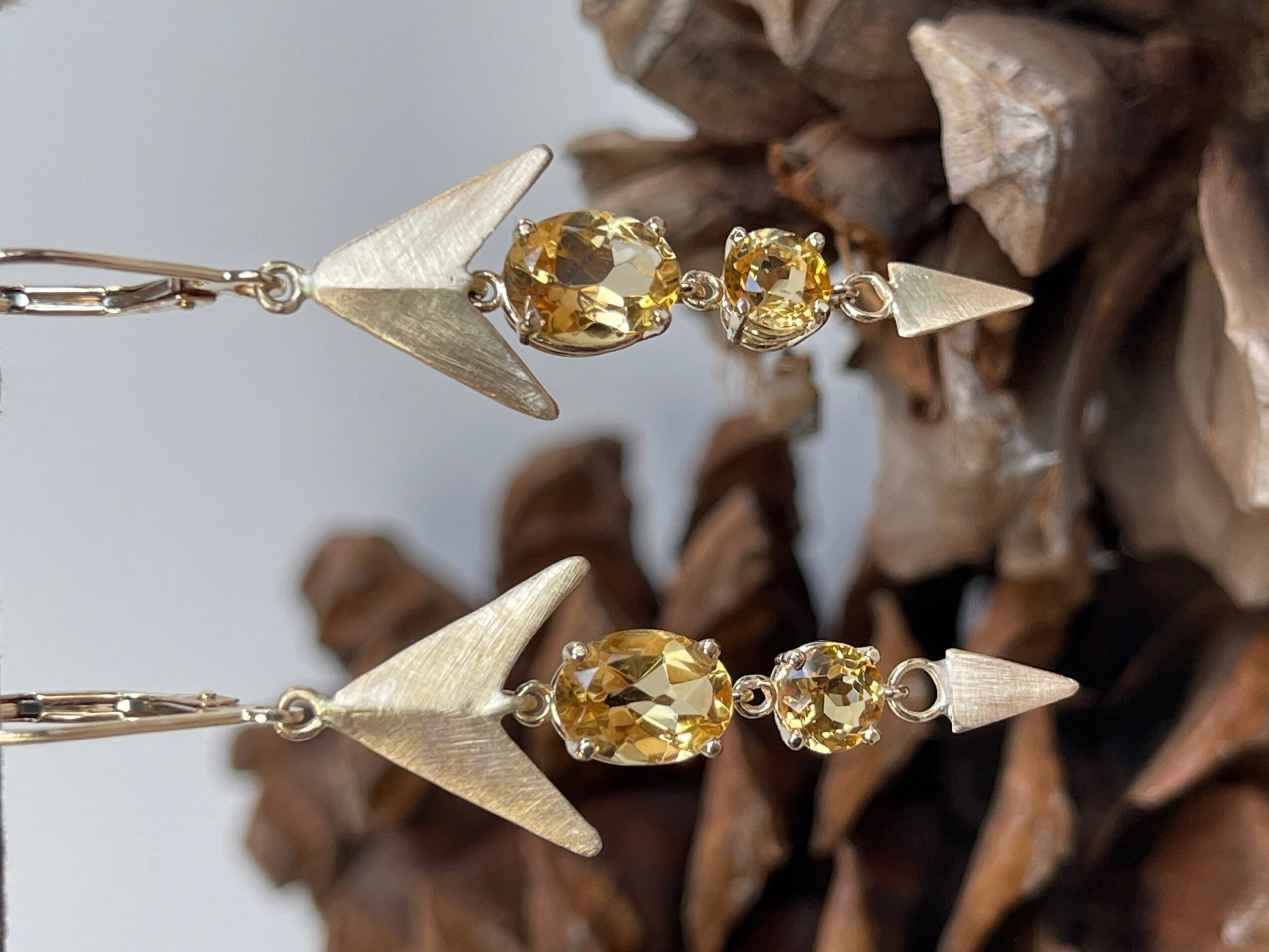 Close-up of a gold and silver earring with yellow gemstones and geometric shapes, against a textured background.